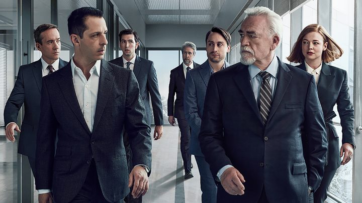 Kendall and Logan Roy walking down a hallway, team members behind them in the show Succession.