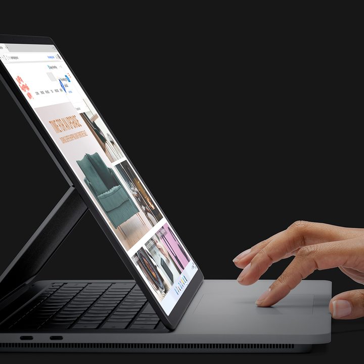 A hand used the touchpad on the Surface Studio Laptop against a black background.