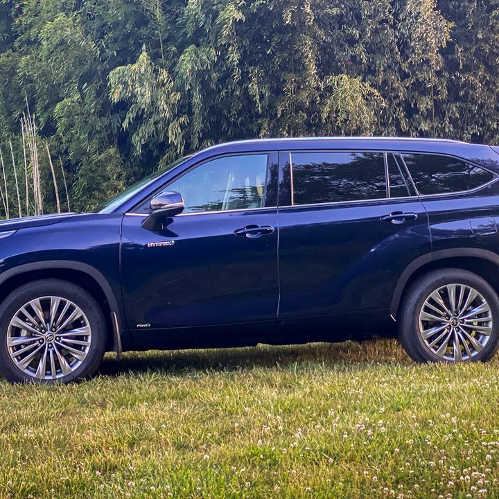 A blue 2021 Toyota Highlander Hybrid in a grassy field with forest in the background.