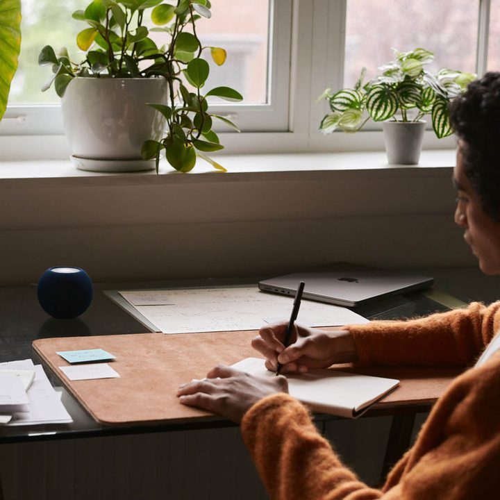 Blue HomePod Mini sitting on desk while person works.