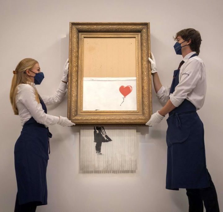 Auction assistants pose with “Love is in the Bin” by British street artist Banksy.