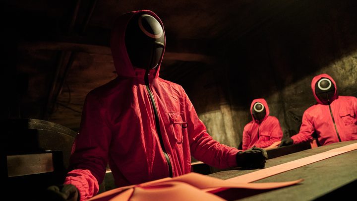 Workers from Squid Game standing over a casket.
