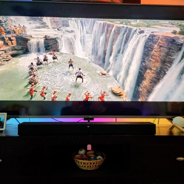 TCL Roku TV Alto R1 Soundbar under a TV on a media stand.