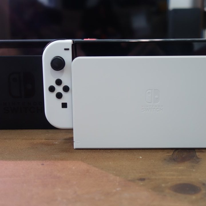 A Nintendo Switch OLED model in its dock next to a regular Switch dock.