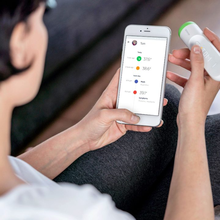 Withings - Thermo Smart Temporal Thermometer being compared with the digital display by a person, over the shoulder view.