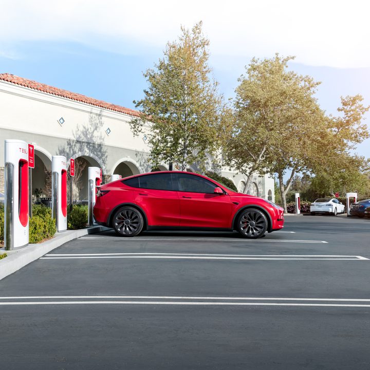 A red Tesla charging at a bank of Tesla Superchargers.