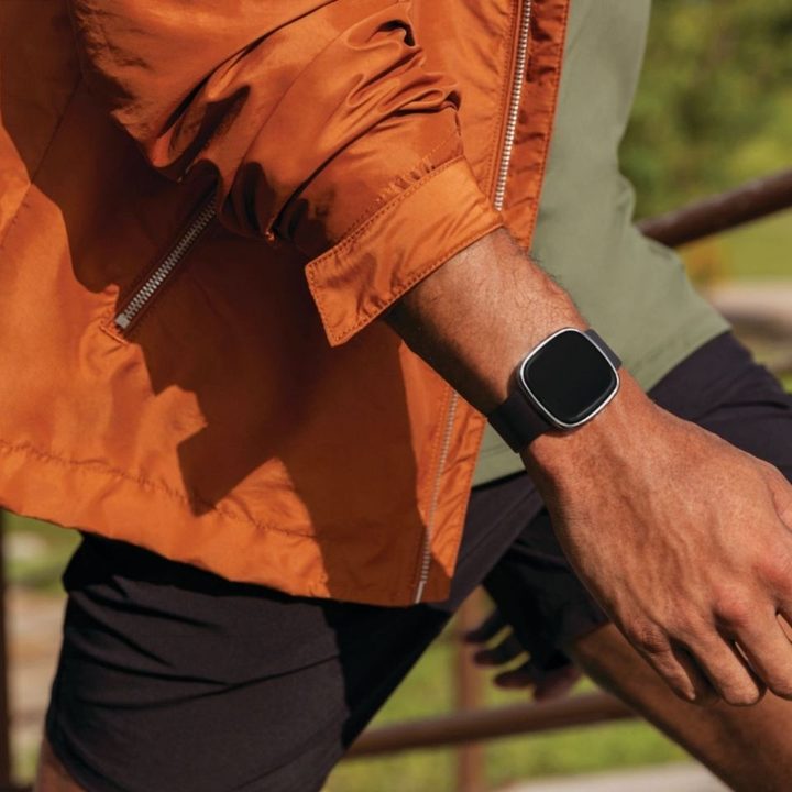 The Fitbit Sense on a man's wrist while he walks outdoors.