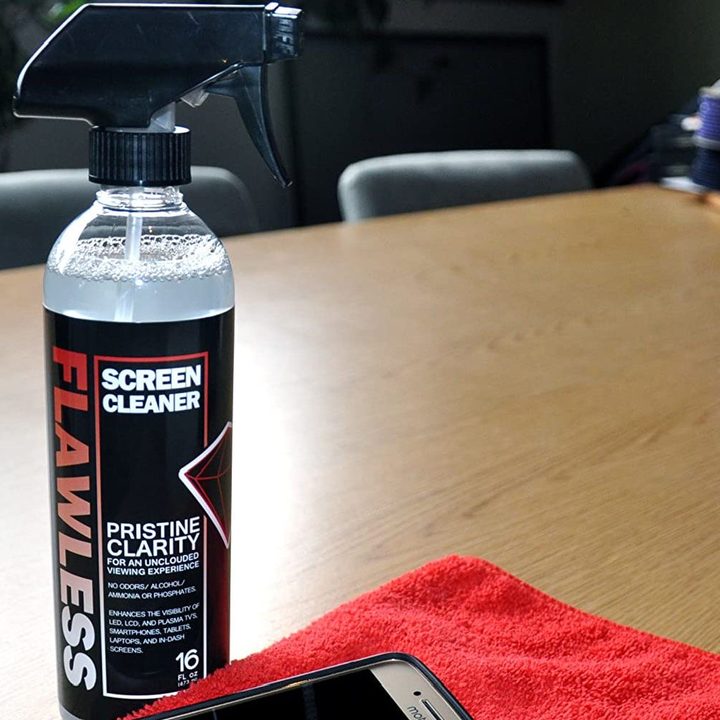 A photo of Flawless screen cleaner next to a red cloth and a smartphone.