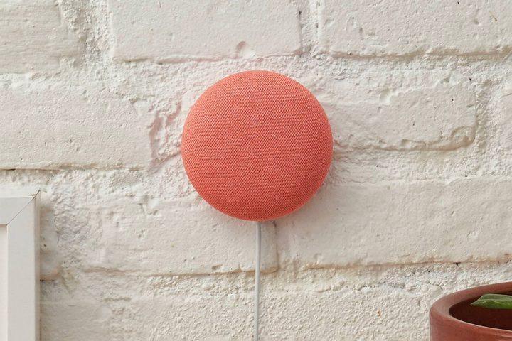 A coral Google Nest Mini mounted on a brick wall.