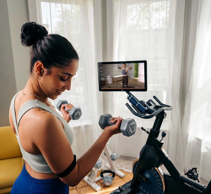 A woman lifting weights in front of the MYX II workout.