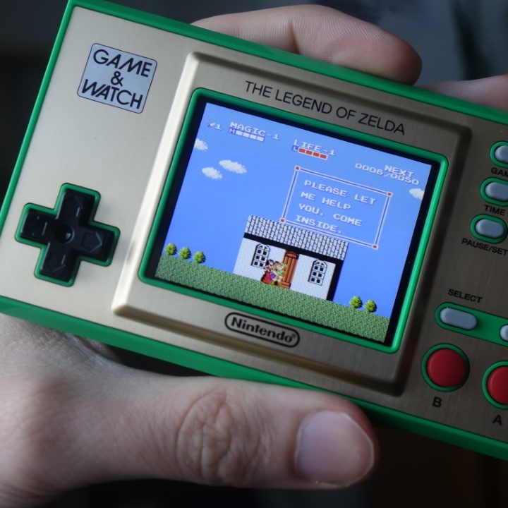 A hand holding the Zelda Game & Watch system.