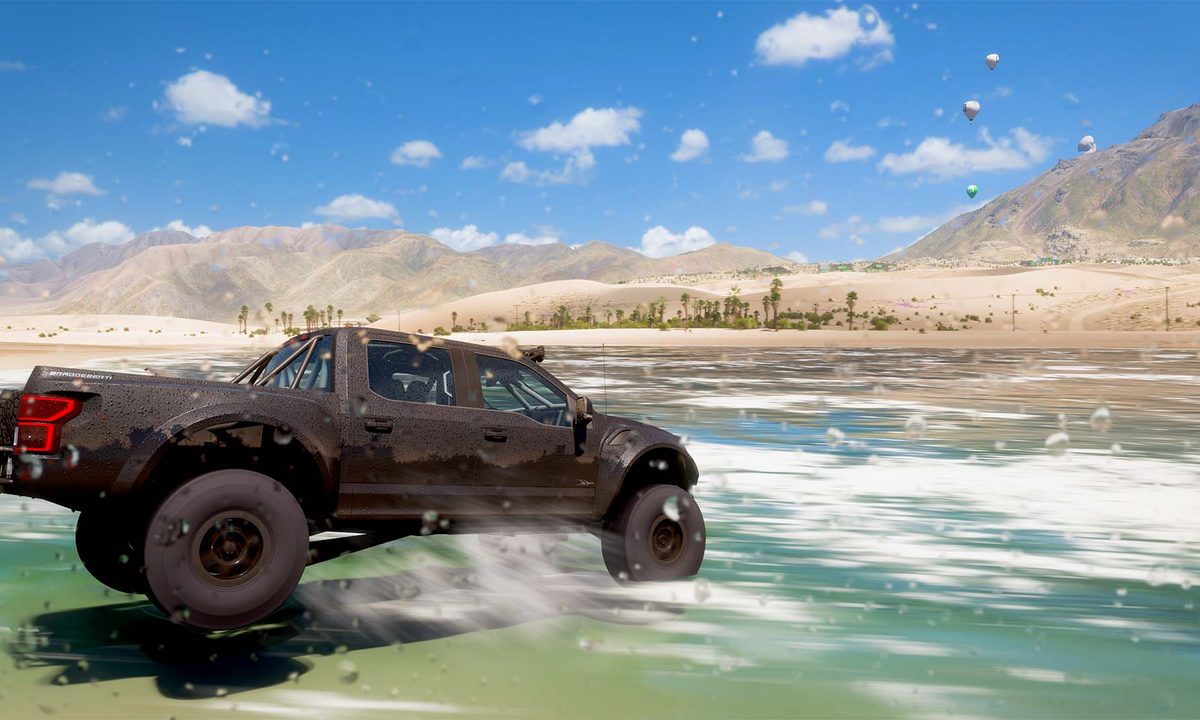 A water splashed picture of a truck driving on the beach on a sunny day.