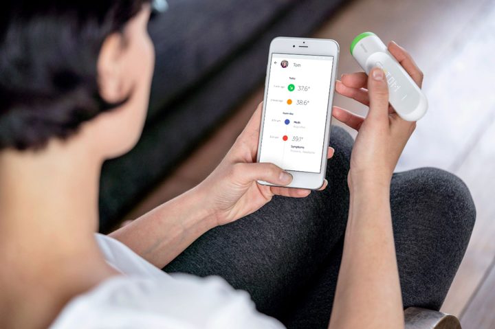 Somebody using a Withings Smart Thermometer with their smartphone.