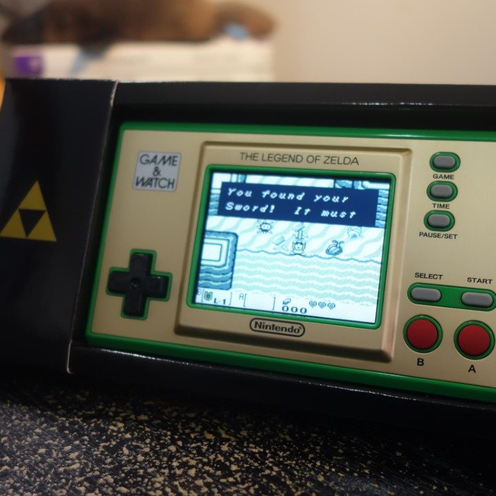 The Zelda Game & Watch sitting in a cardboard stand.