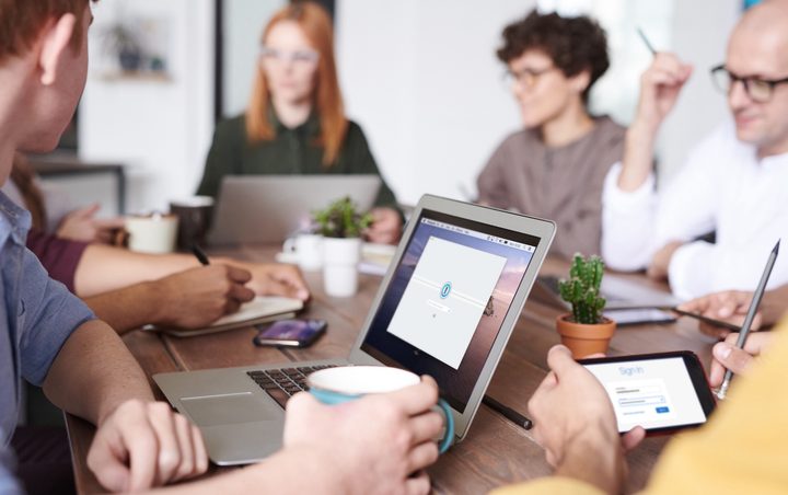 A group of people sitting at a desk looking at 1Password displayed on a screen.