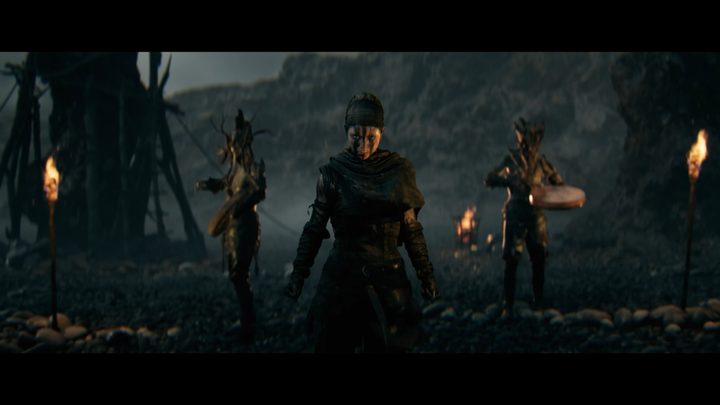 Senua stands ready near some drummers.