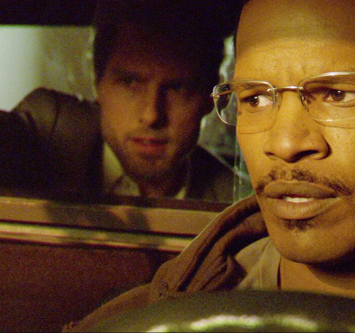 Tom Cruise sits in the back of a taxi with Jamie Foxx driving in Collateral.