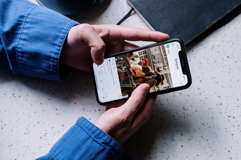 A person seated at a table scrolls through their instagram timeline.