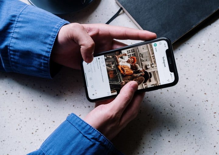 A person seated at a table scrolls through their instagram timeline.