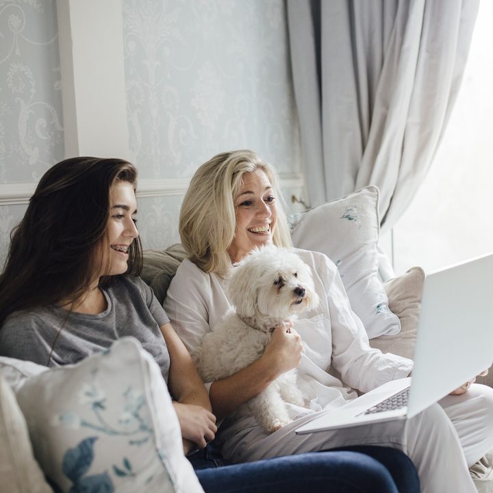 Two women video calling on their laptop with dog nearby protected by McAfee.