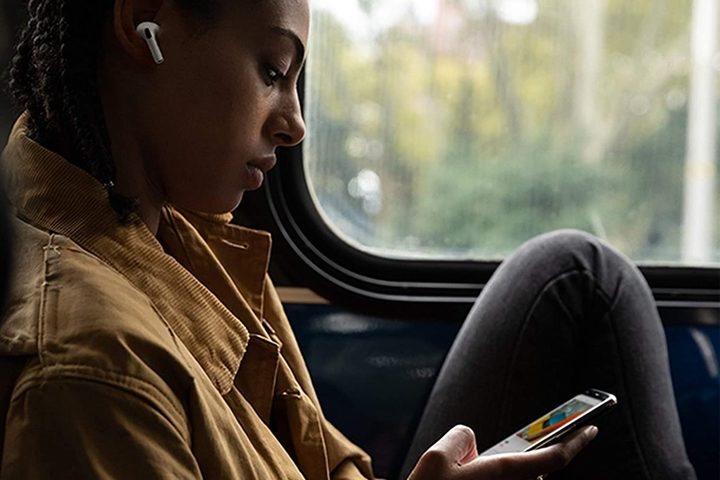 A person sitting on a train wearing New Apple AirPods Pro while looking at a phone.