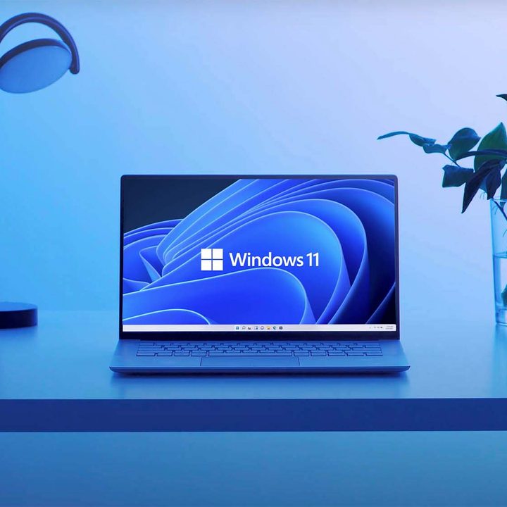 A laptop sits on a desk with a Windows 11 wallpaper.