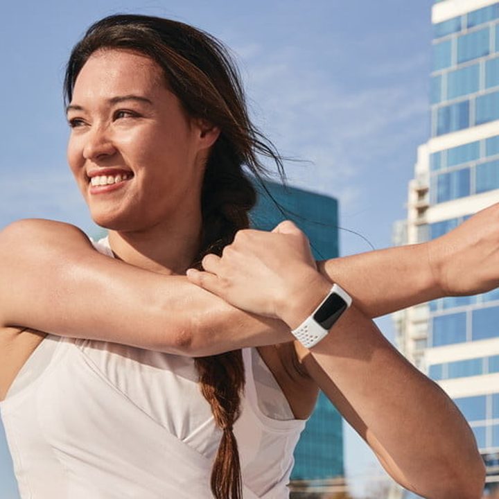A woman wearing a Fitbit Charge 5 stretching her shoulder during a workout.