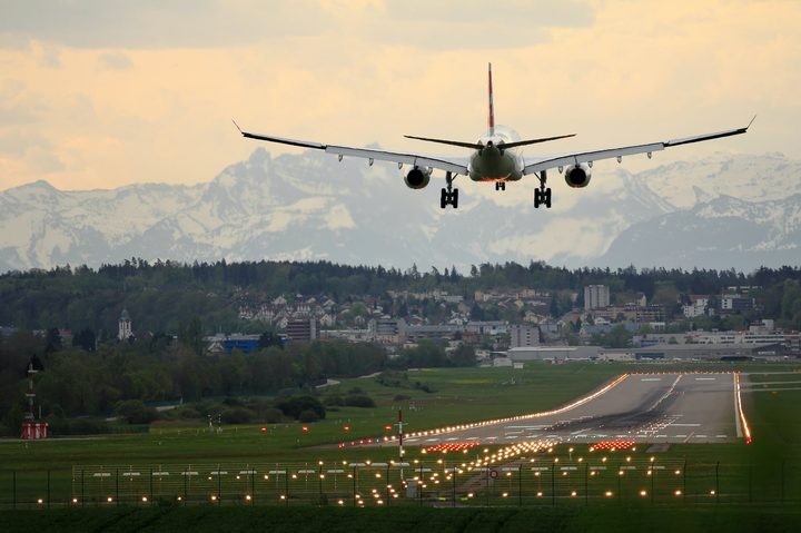 Aircraft coming in for a landing at dusk over a runway with Swiss Alps in the background.