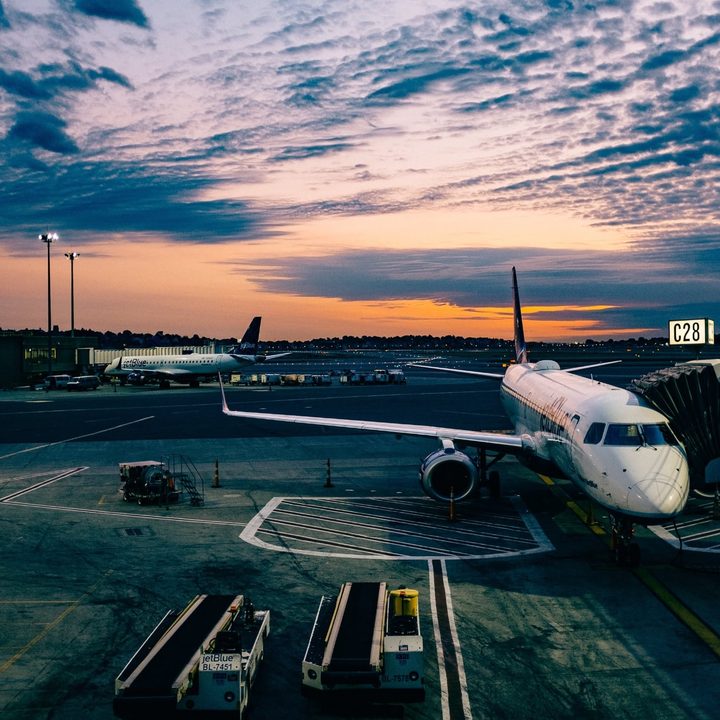 Aircraft parked on airport tarmac as the sun sets in the background.