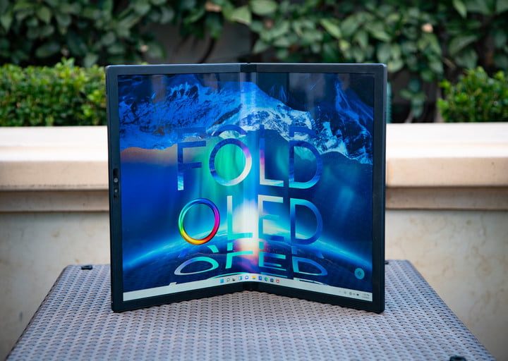 The Aus Zenbook 17 Fold folded in half on a table in front of some hedges.