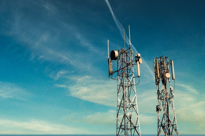 Two tall cellular microwave radio towers against a blue sky.