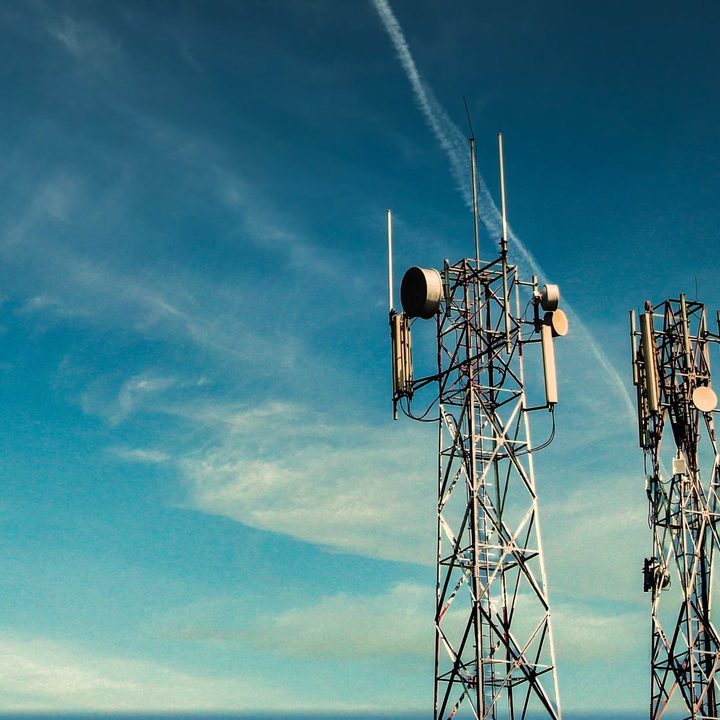 Two tall cellular microwave radio towers against a blue sky.