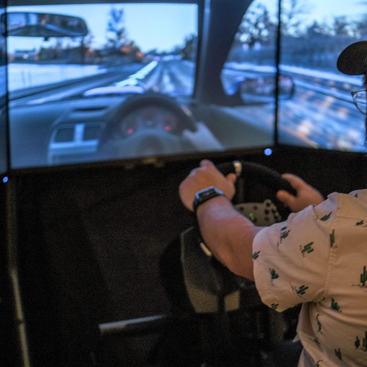 A player drives in Forza using Monoprice's pro racing wheel on three monitors.