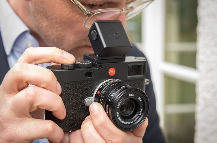 A man peers through the viewfinder of the Leica M11.