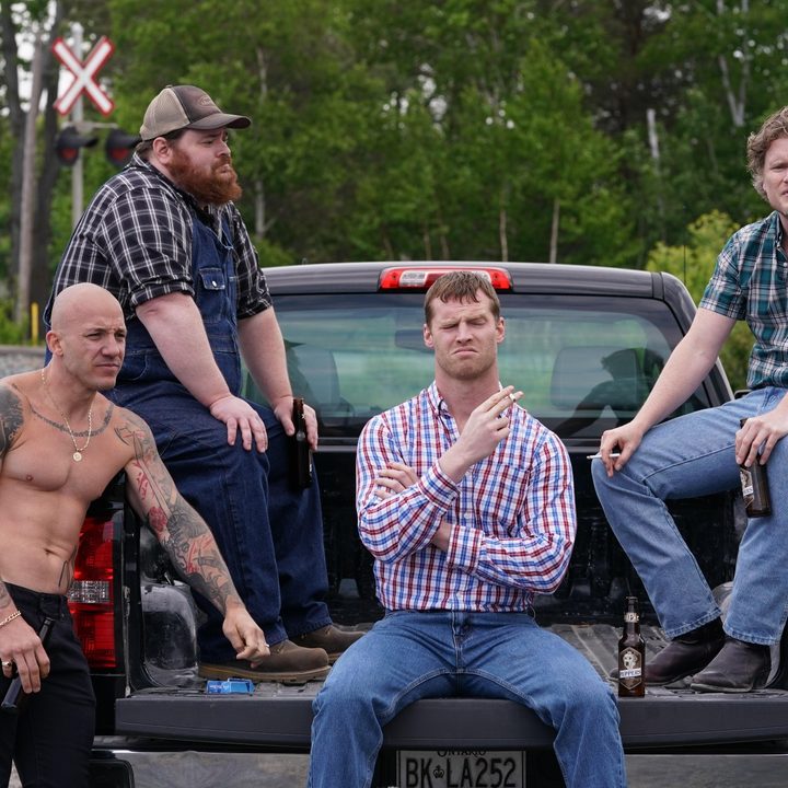Actors from the cast of Letterkenny seated in the back of a pickup truck.