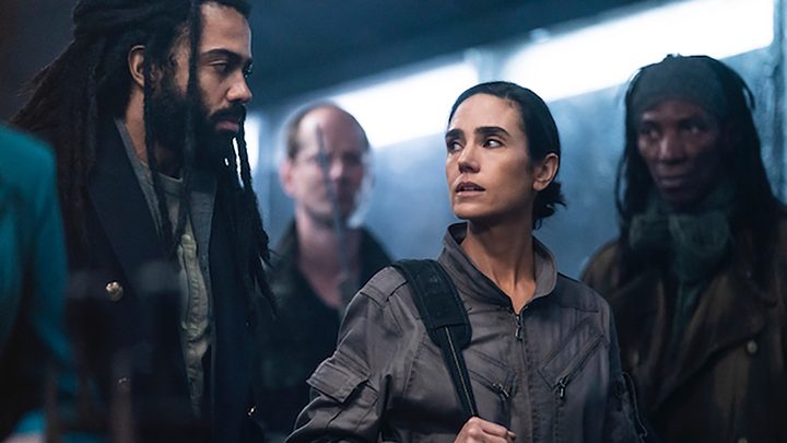 David Diggs and Jennifer Connelly stare at one another, two people behind them in a scene from Snowpiercer.