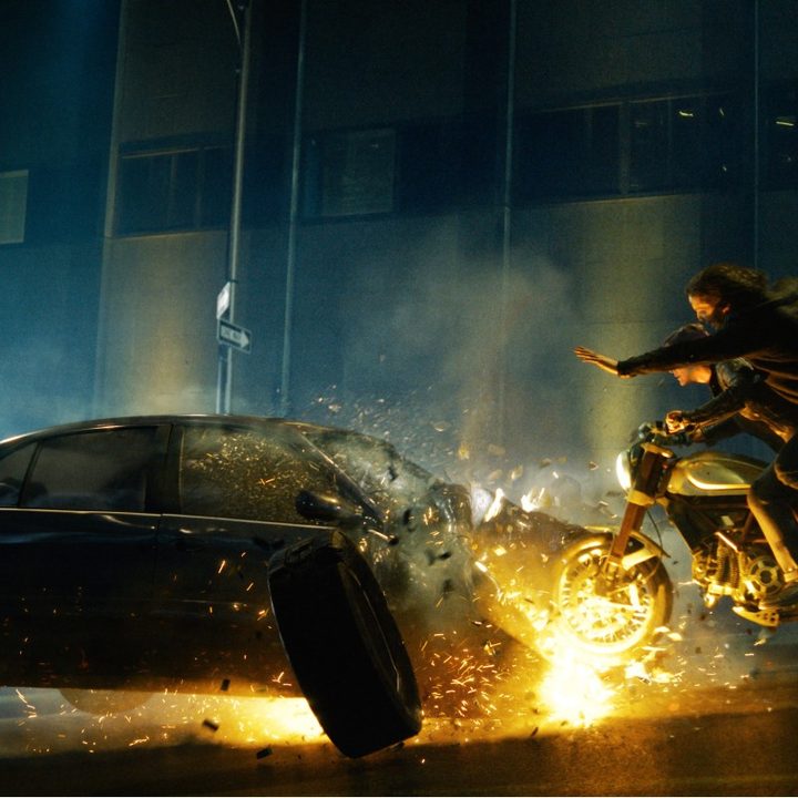 Keanu Reeves and Carrie-Anne Moss ride a motorcycle in an explosive scene from The Matrix Resurrections.