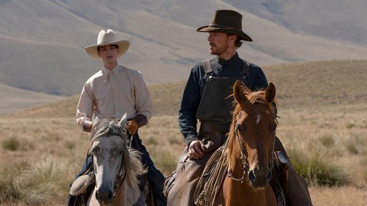 Two cowboys ride horses in a field in The Power of the Dog.