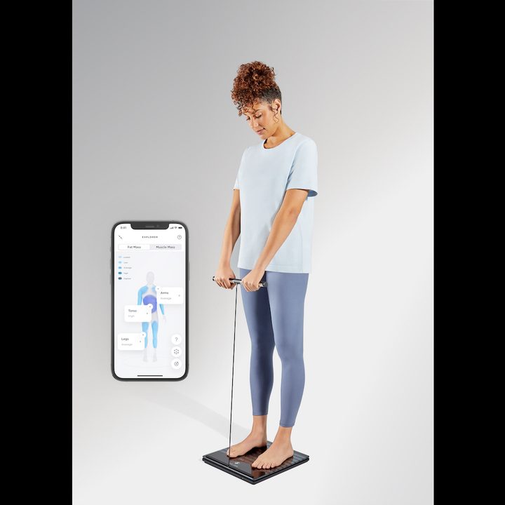 Woman using Withings Body Scan scales with handle while accompanying app displaying health information.