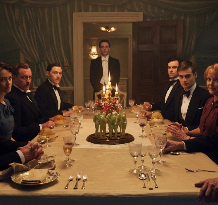Guests seated at a dining table look at the camera in And Then There Were None.