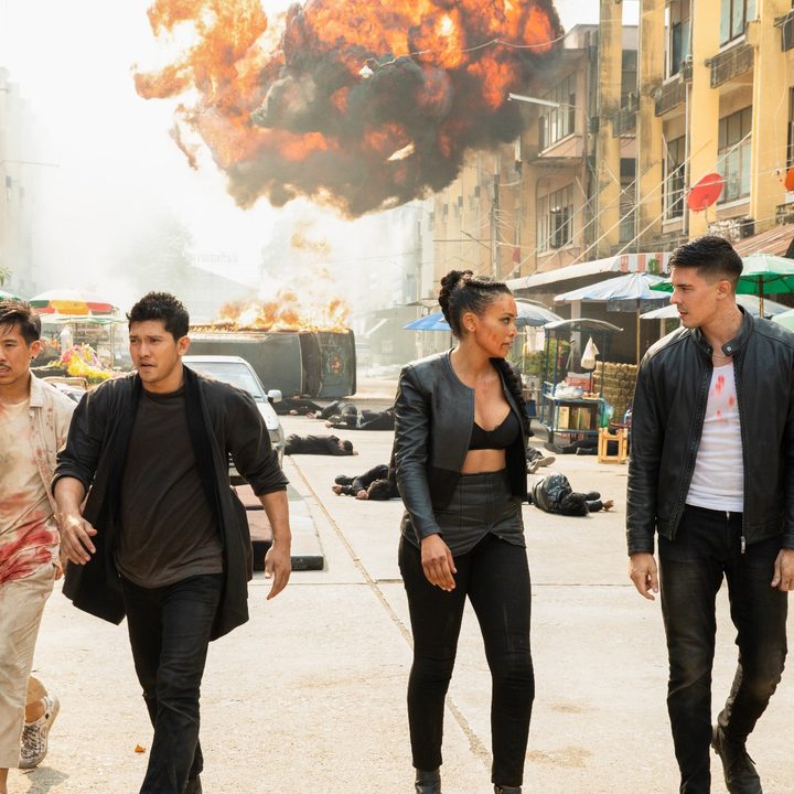 Characters from Fistful of Vengeance walk down the street as a car explodes behind them.
