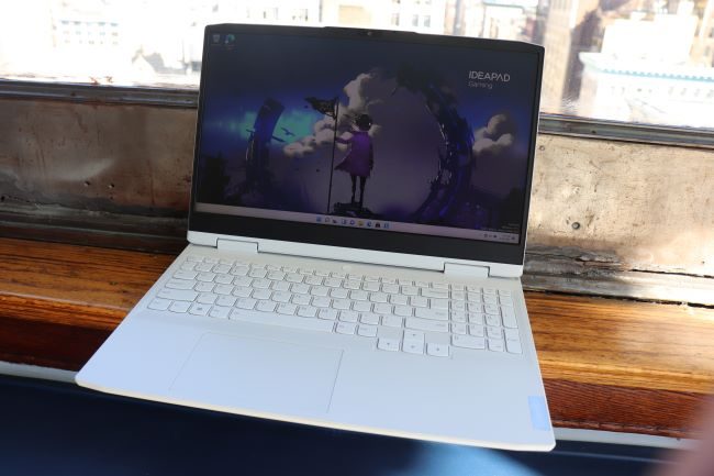 The white 15-inch IdeaPad Gaming 3 is placed on a seating area near a large window.