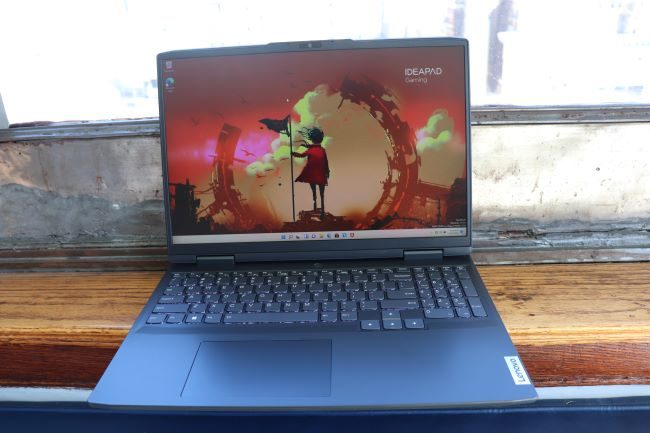 The black 16-inch IdeaPad Gaming 3 is placed on a seating area near a large window.