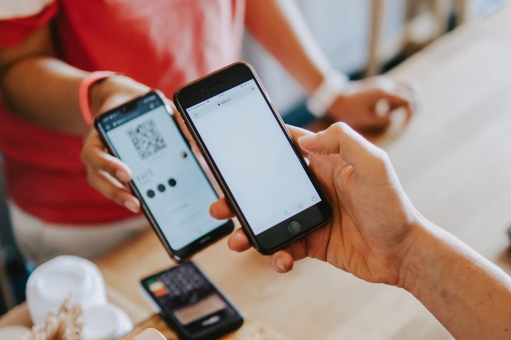 Person holding a smartphone over another smartphone at a retail counter.