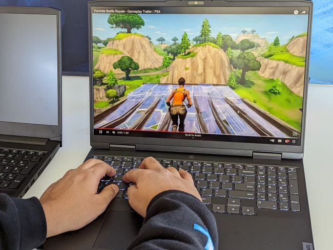 A video game trailer being played on the black 16-inch IdeaPad Gaming 3 while hands are typing on the keyboard.