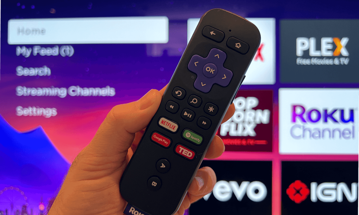 Roku remote in hand with Roku home screen in. the background.