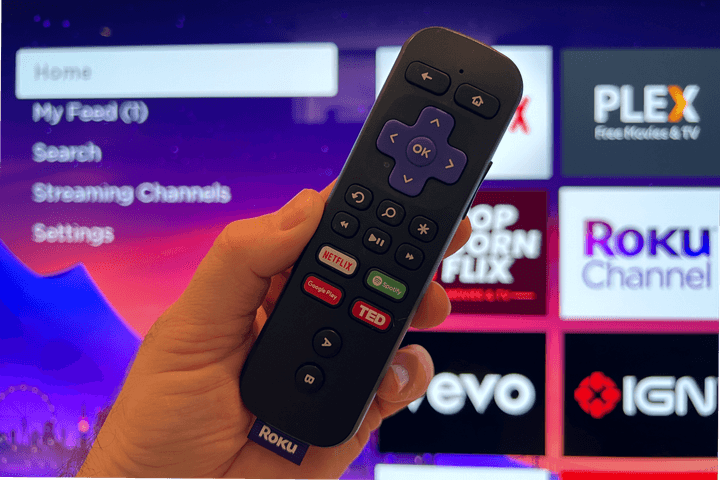 Roku remote in hand with Roku home screen in. the background.
