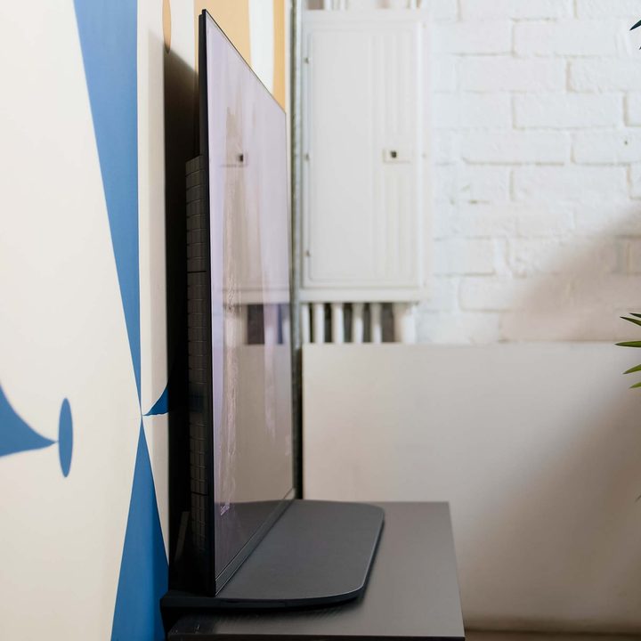 A side view of the thin Sony A95K TV sitting on a media stand against a wall.