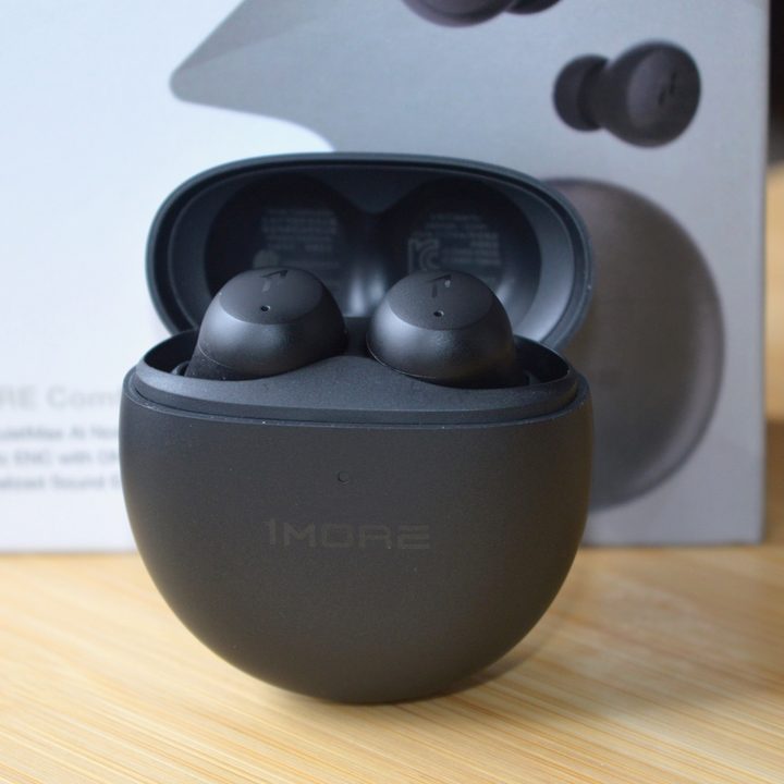 Front view of the 1More ComfoBuds Mini inside their charging case, with the packaging in the background.