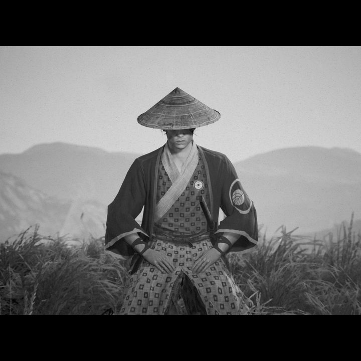 Hiroki sits in thought in a field with mountains in the background in Trek to Yomi.
